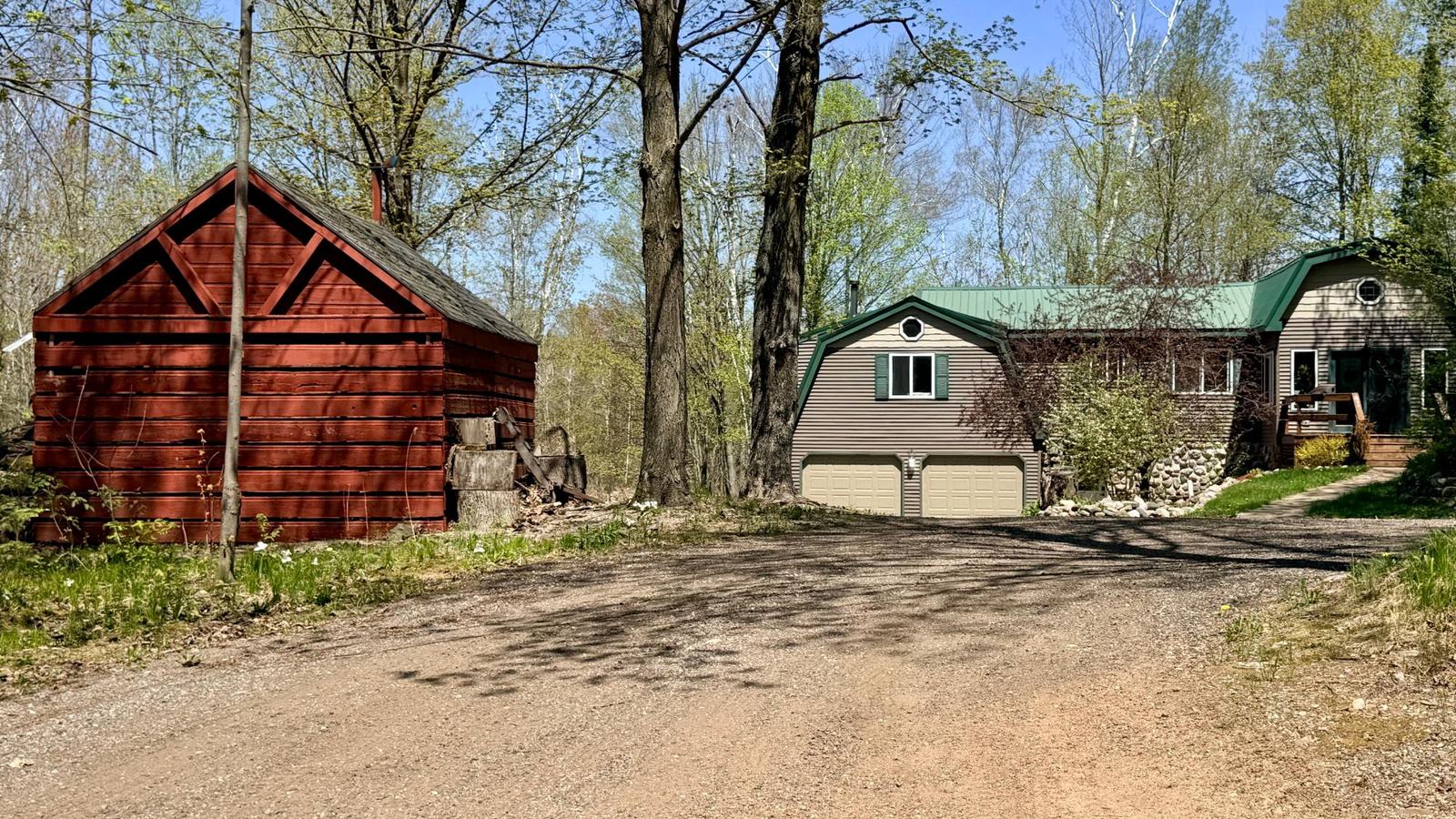 Wide view of the home and attached garage among spring trees, gravel driveway in foreground