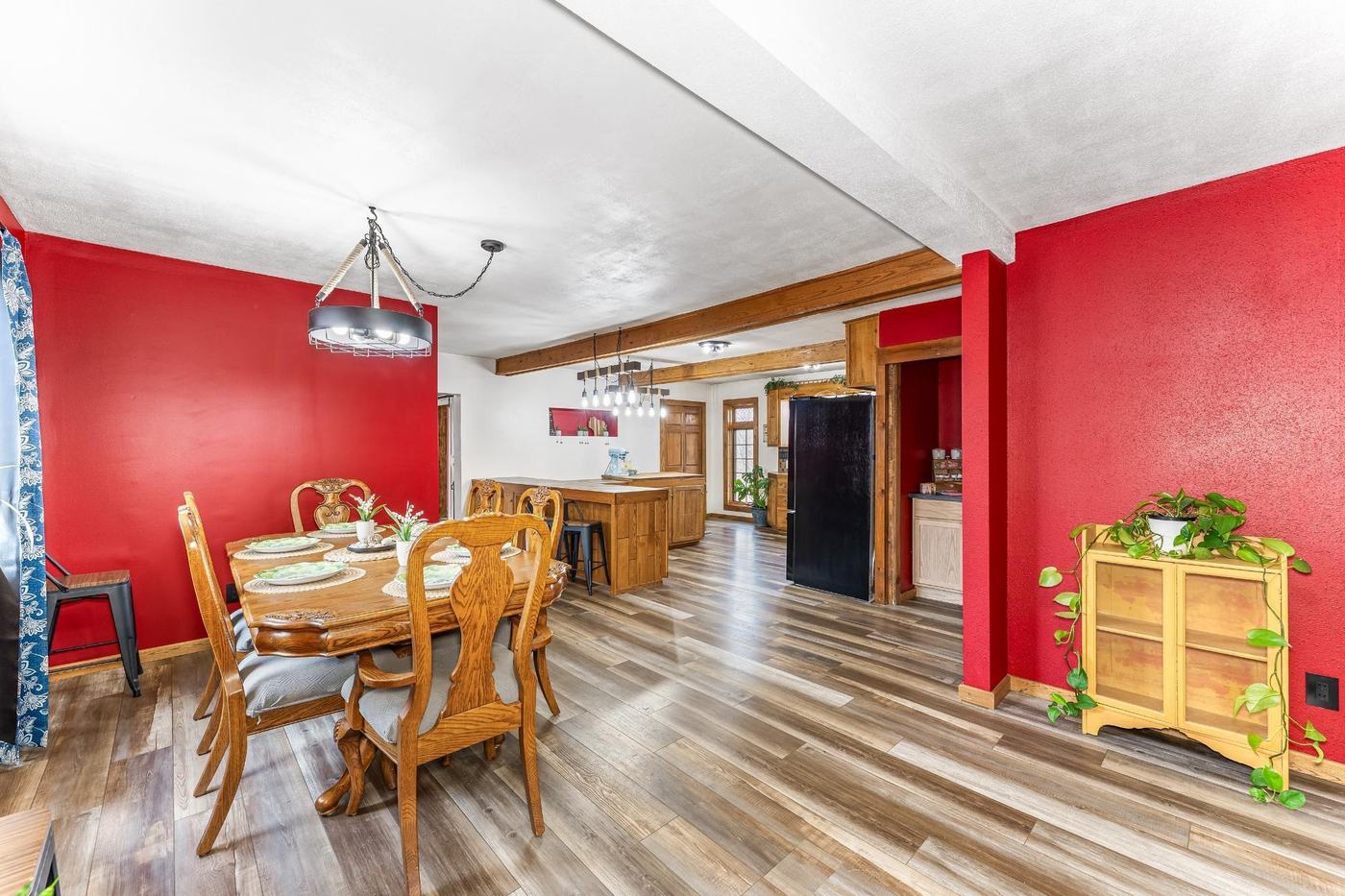 Open dining room with a red accent wall, wood table set for four, and sightline into the kitchen