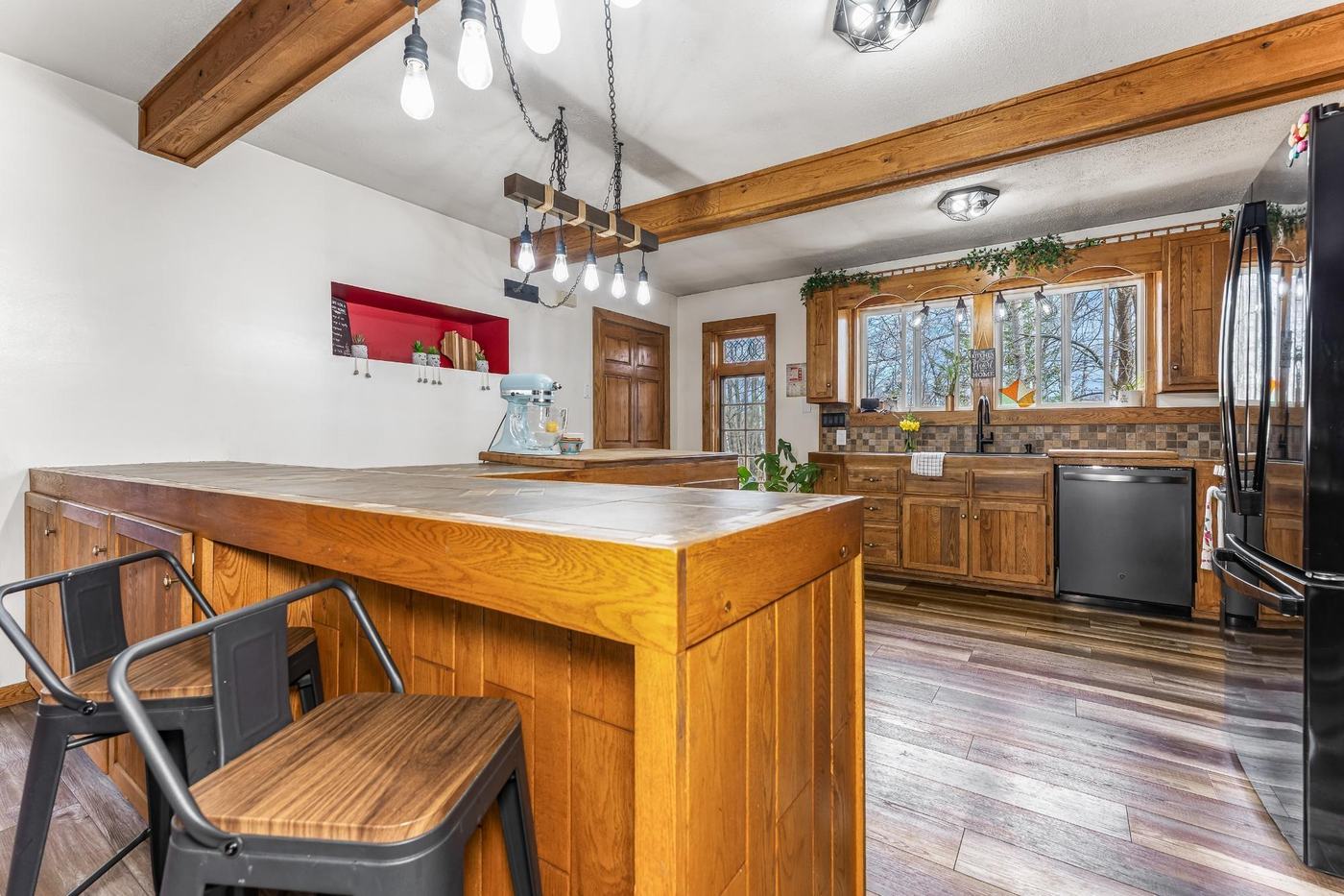 Kitchen island with tile countertop and pendant lighting, black bar stools in foreground