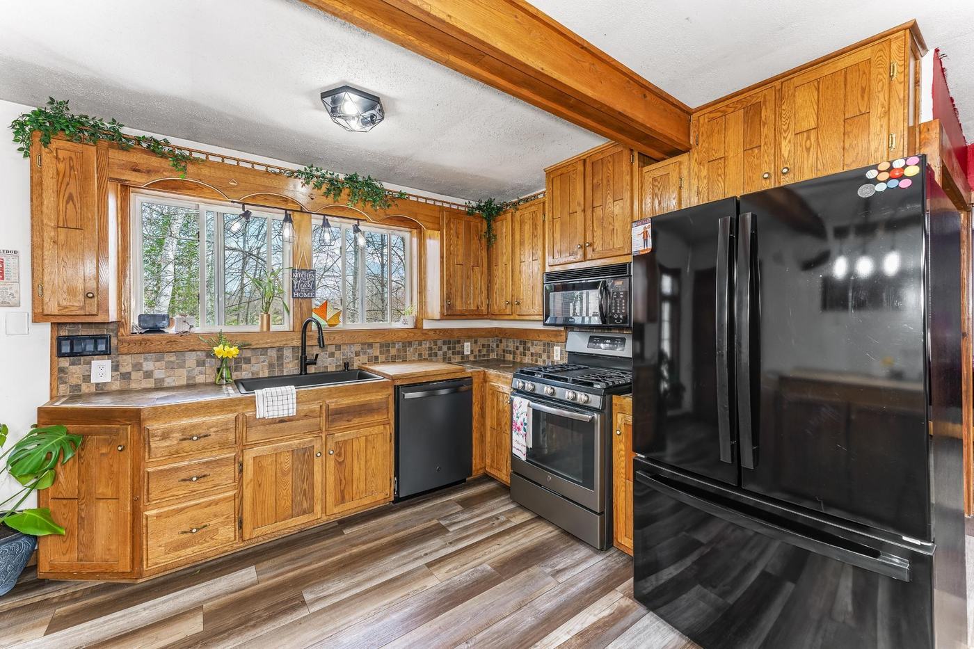 Kitchen with oak cabinetry, black appliances, and a window over the sink framed by tile backsplash