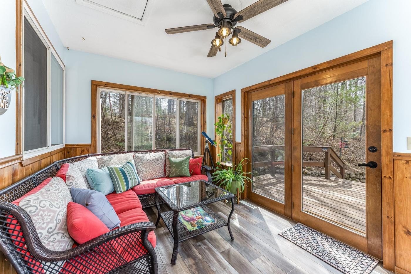 Sunroom with wicker sectional, red cushions, and glass doors opening onto a wooded deck