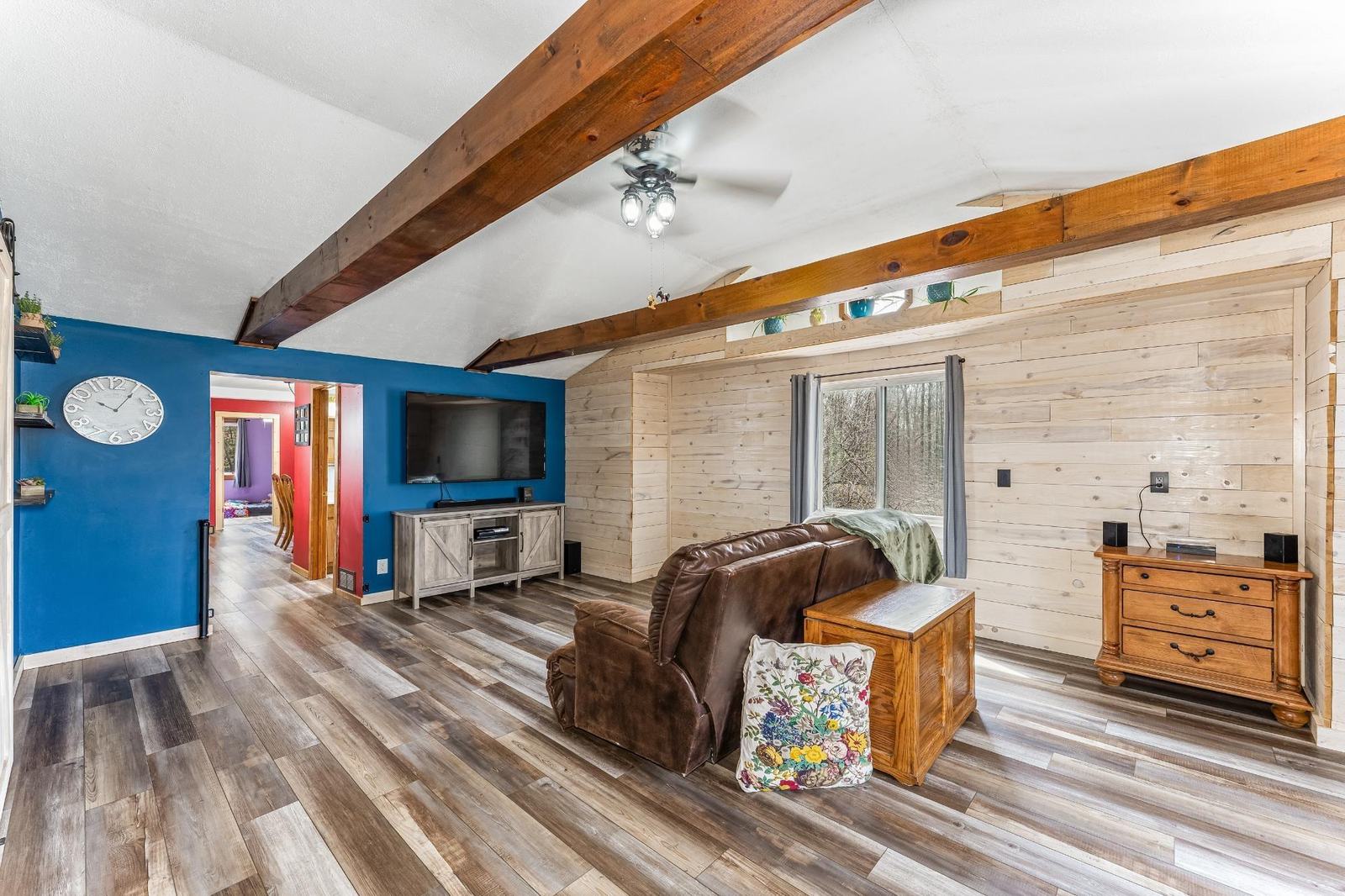 Vaulted living room with exposed wood beam ceiling, blue accent wall, and a leather sofa