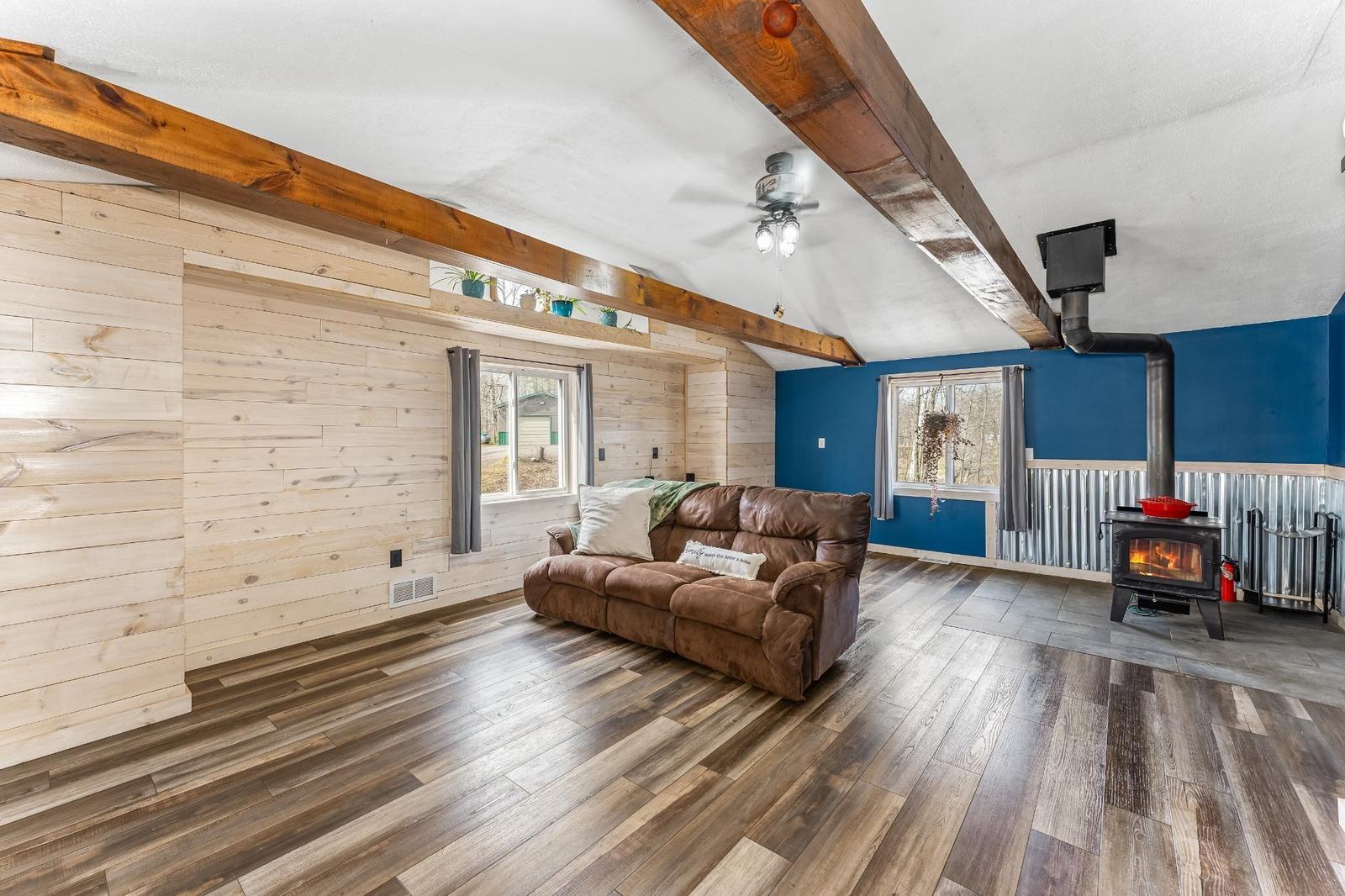 Lower level family room with a wood stove, corrugated metal wainscoting, and a leather reclining sofa