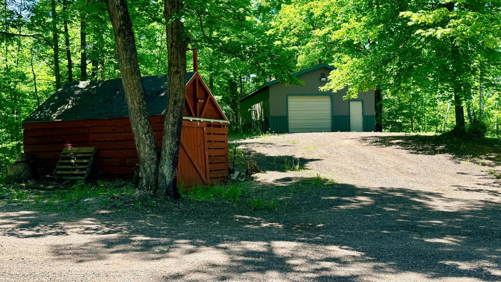 Workshop building tucked into summer trees with a log storage shed in front