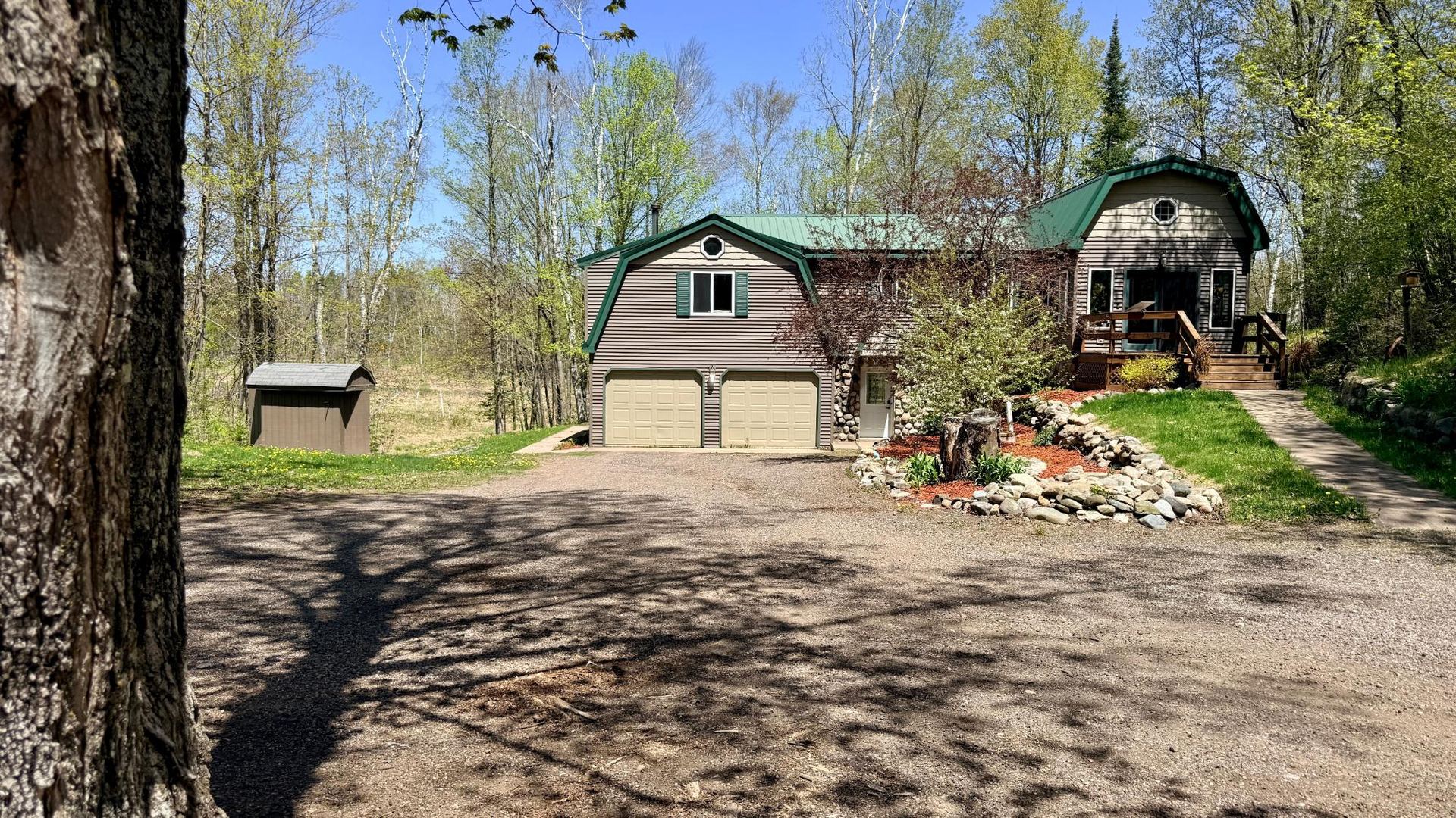 Northwoods home with green metal roof, seen from the gravel driveway through spring trees